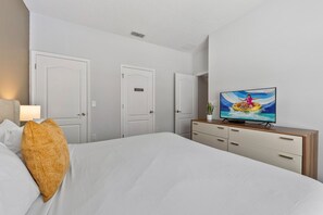 A hotel room with a bed, a television, a wooden dresser, and two doors.