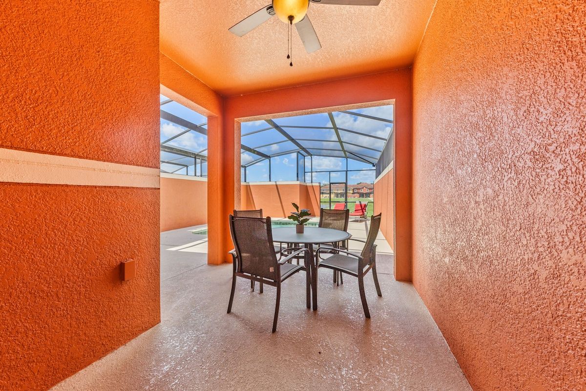 Ein überdachter Patio-Bereich mit Tisch und Stühlen, einem Deckenventilator und Blick durch eine transparente Dachkonstruktion.
