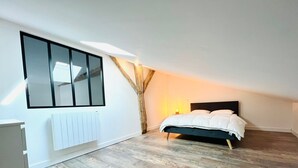 Um quarto com cama, radiador, janela e uma viga de madeira.