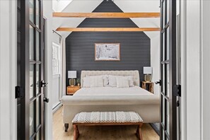 A bedroom with a large bed, bedside tables, a bench, and a framed picture on the wall.