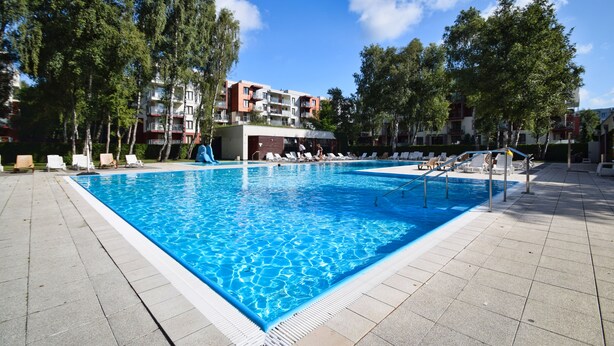 A rectangular swimming pool with clear blue water, surrounded by lounge chairs and a tiled deck. - RentPlanet - Apartament Klonowa (Kołobrzeg)