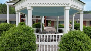 Um gazebo com exterior branco e teto verde, rodeado por vegetação e um cercado branco.