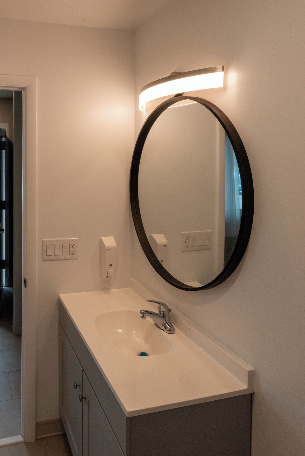 Un baño con un lavabo blanco, un espejo redondo y una lámpara sobre el espejo.
