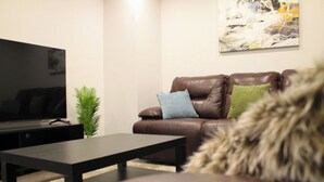 A living room with a leather sofa, a television on a stand, and a small plant. - Luxury 2 bedroom basement (Winnipeg)
