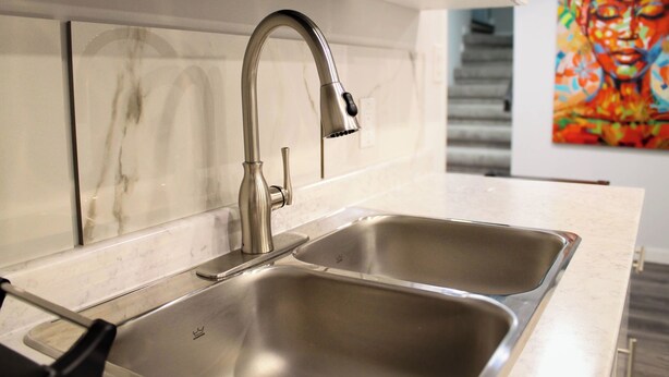 A modern kitchen with a stainless steel sink and faucet, marble backsplash, and a colorful painting on the wall. - Luxury 2 bedroom basement (Winnipeg)