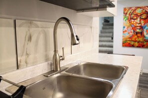 Una cocina moderna con un lavamanos y grifo de acero inoxidable, un salpicadero de mármol y un cuadro de colores en la pared.