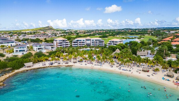 A coastal resort with multiple hotel buildings, a sandy beach, and clear turquoise waters.
