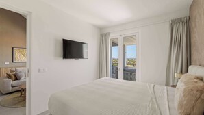 A modern hotel room with a bed, a television, a sofa, and a balcony with curtains.