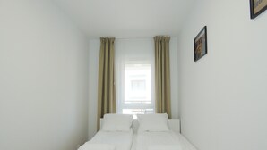 A small, clean room with two single beds, beige curtains, and a framed picture on the wall. - RentPlanet - Apartament Górczyńska (Poznań)