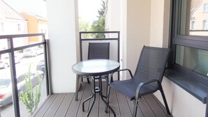 A balcony with a round glass table and two chairs, a view of parked cars, and buildings in the background. - RentPlanet - Apartament Górczyńska (Poznań)