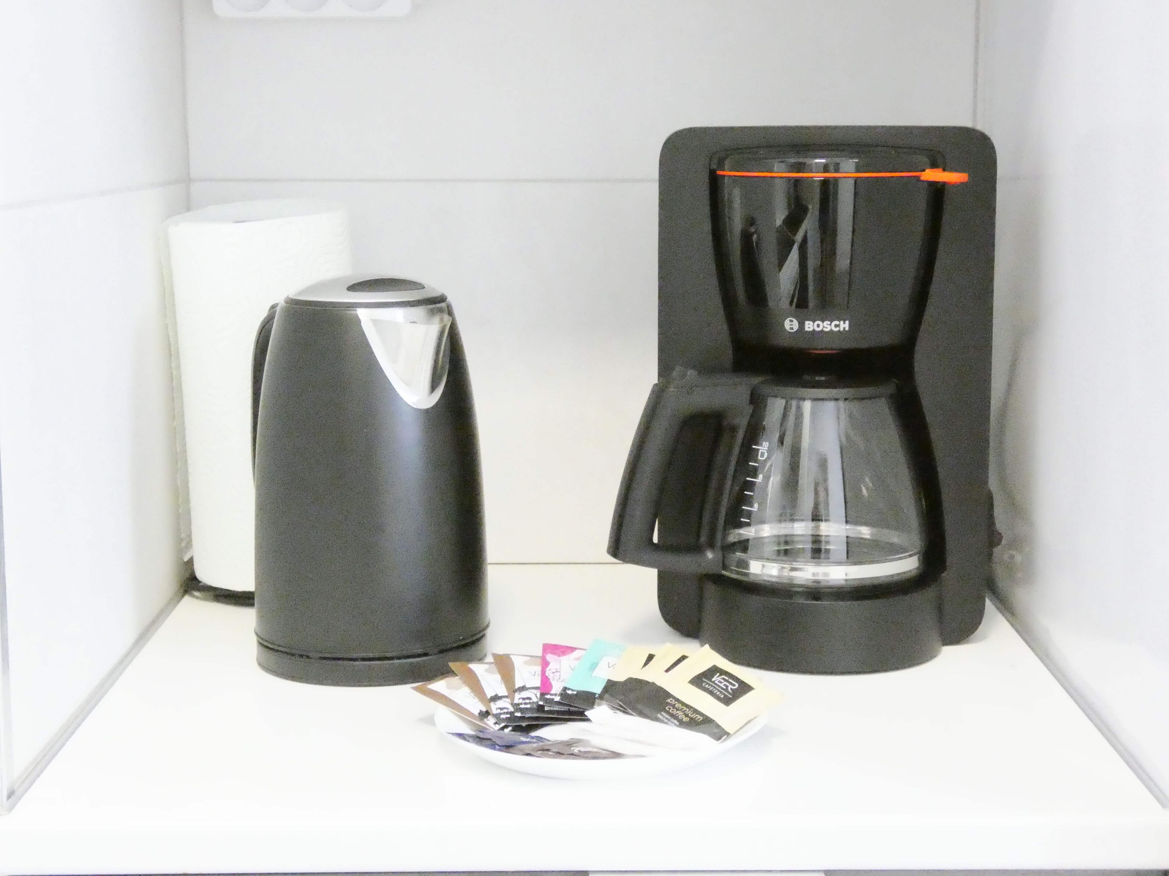 Eine Kaffeemaschine und ein Wasserkocher auf einer weißen Arbeitsplatte.
