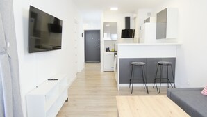 A modern, compact living space with a TV mounted on the wall, a kitchenette area, and a seating area with two stools. - RentPlanet - Apartament Górczyńska (Poznań)