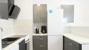 A compact kitchen with a dishwasher, a coffee maker, and a refrigerator. - RentPlanet - Apartament Górczyńska (Poznań)