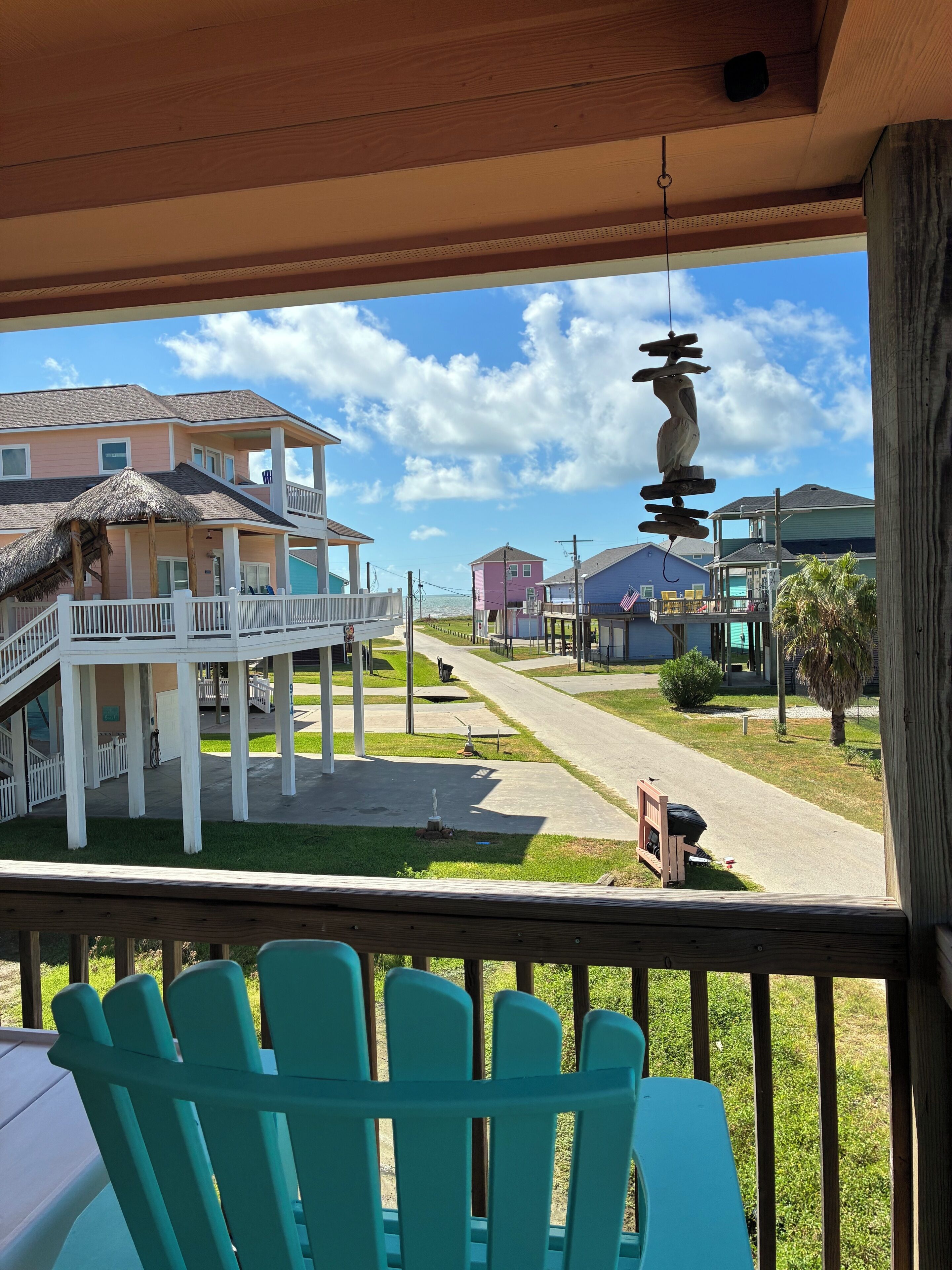 A balcony with teal chairs, a view of a street with houses, and a hanging bird sculpture.