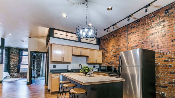A modern kitchen with a large island, stainless steel appliances, and a brick wall. - 2BR-1BA, Sleeps 4 | Downtown Ames (Ames)