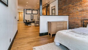 A modern bedroom with a brick wall, wooden flooring, a bed, a dresser, and a seating area with a table and chairs. - 2BR-1BA, Sleeps 4 | Downtown Ames (Ames)