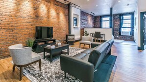 A modern living room with a brick wall, a flat-screen TV, a fireplace, and a large sofa. - 2BR-1BA, Sleeps 4 | Downtown Ames (Ames)