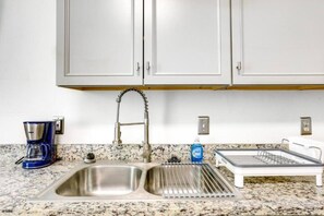 Una cocina con un lavamanos doble, una cafetera, un escurreplatos y un grifo de acero inoxidable.