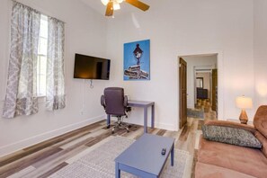 Una sala de estar con televisión, escritorio, silla, sofá y lámpara.