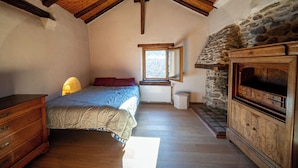 A bedroom with a wooden ceiling, a stone fireplace, a bed with a quilt, a dresser, and a window with a view. - Mountain house near Méribel (Brides-les-Bains)
