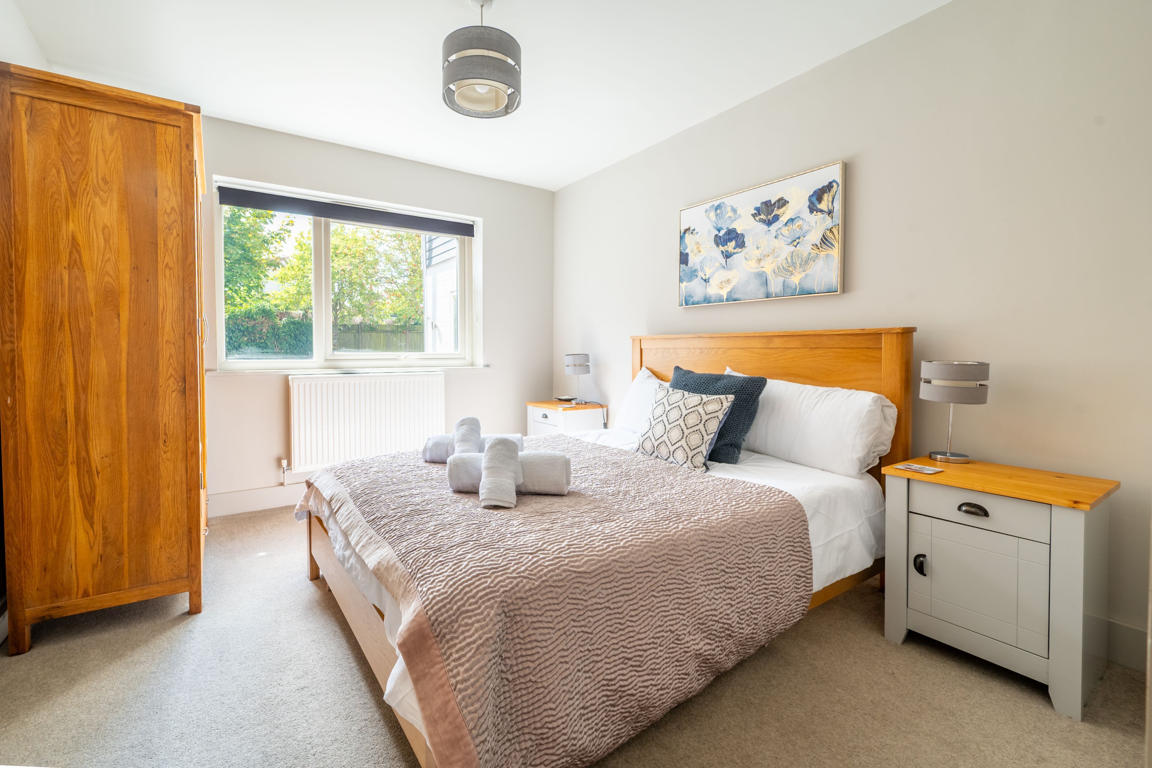 A bedroom with a large bed, a wooden wardrobe, a bedside table with a lamp, and a window with blinds.