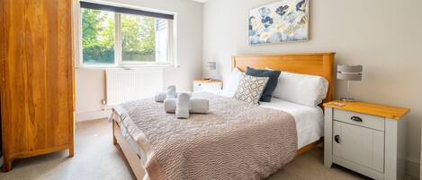 A bedroom with a large bed, a wooden wardrobe, a bedside table with a lamp, and a window with blinds.
