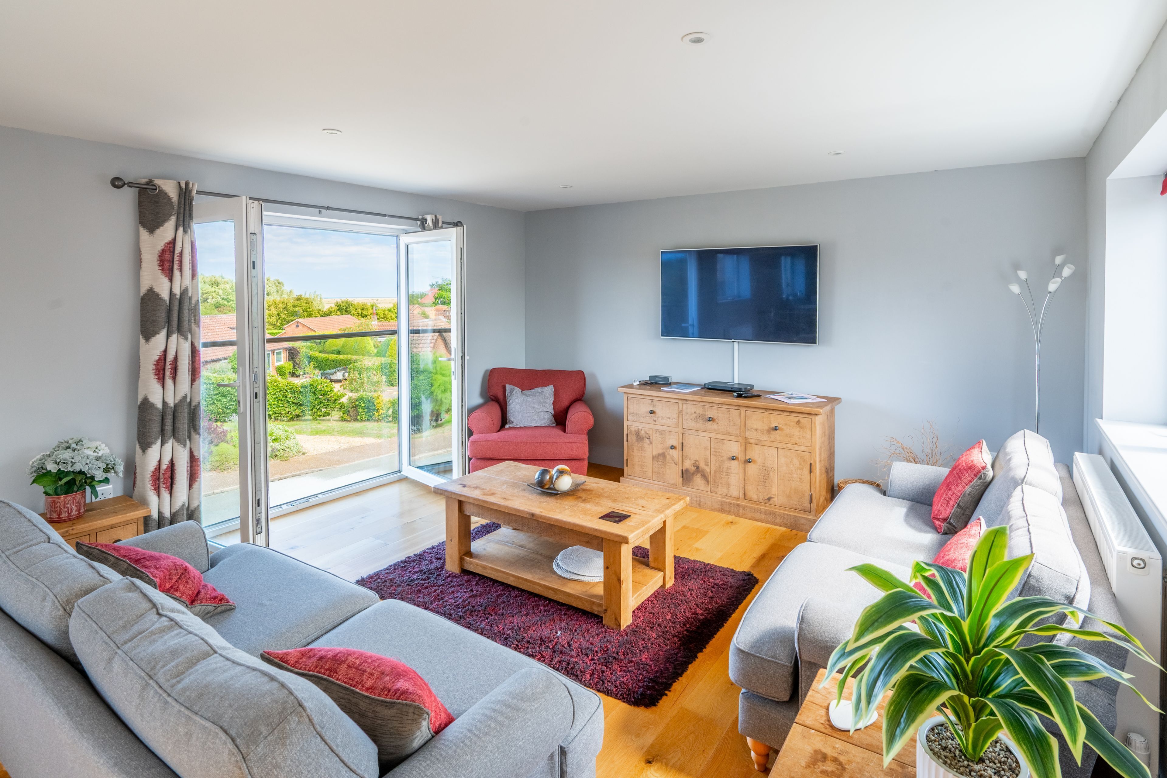 A modern living room with a sofa, a red armchair, a wooden coffee table, and a TV on the wall.