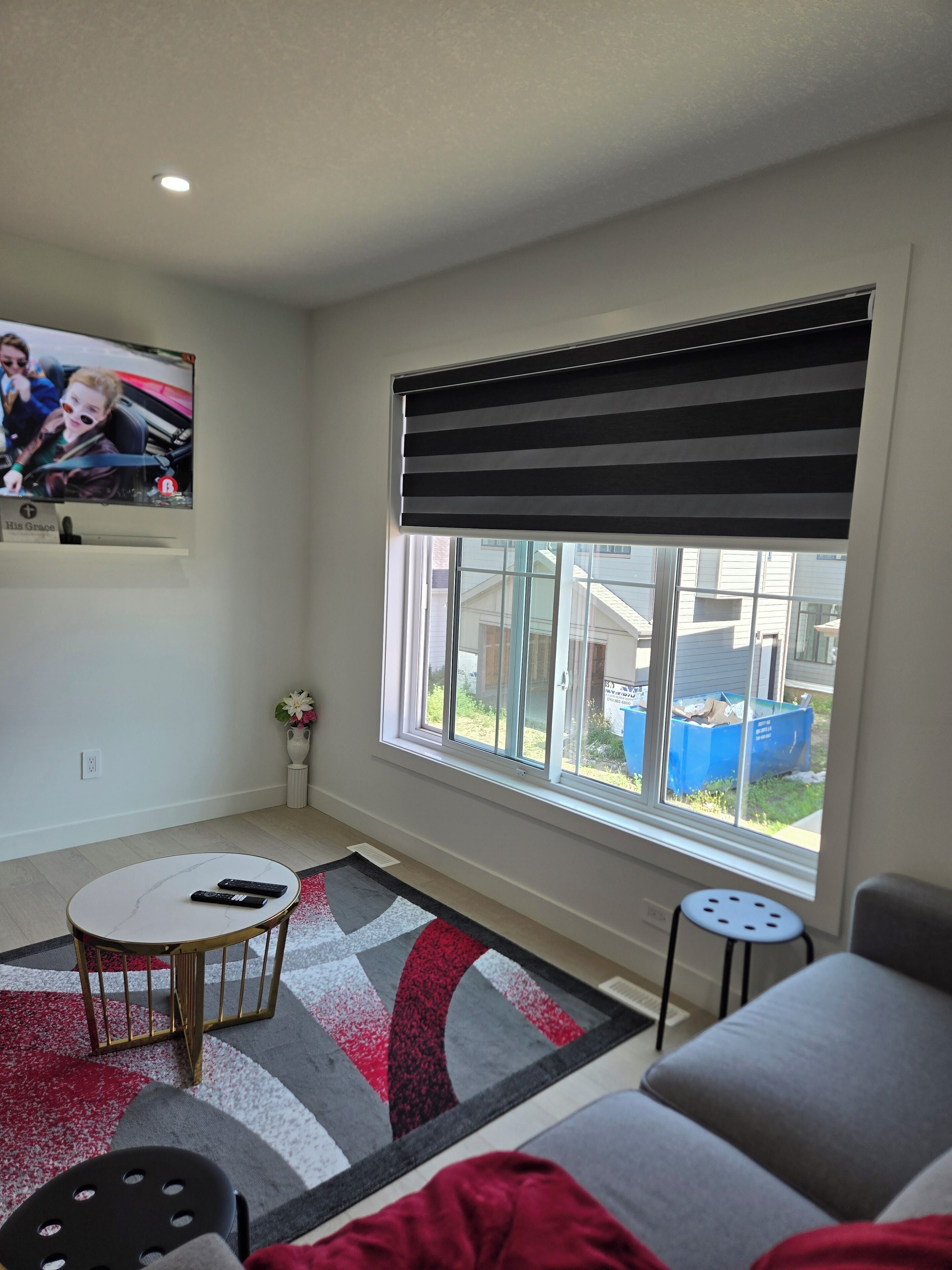 A living room with a large window, a television mounted on the wall, a round coffee table, and a sofa.