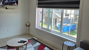 Una sala de estar con un ventanal grande, un televisor montado en la pared, una mesa redonda de centro y un sofá.