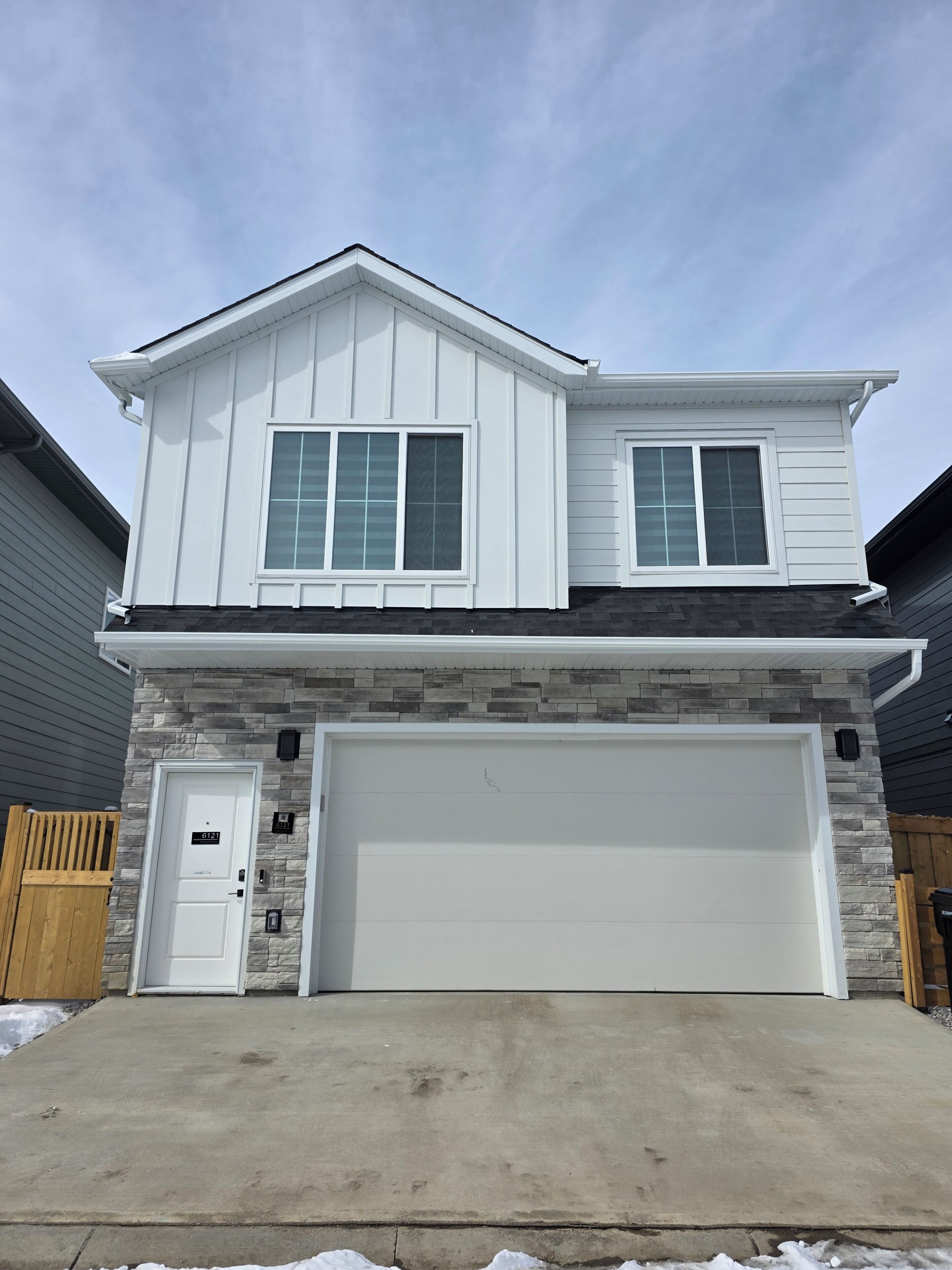 A two-story house with a garage, a stone facade, and a wooden door.