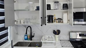 Una cocina compacta con muebles blancos, estufa integrada, un lavamanos y una encimera con diversos utensilios de cocina.