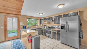 A modern kitchen with stainless steel appliances, a built-in oven, and a refrigerator. There is a window providing natural light and a door leading to an outdoor area.