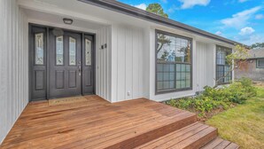 A modern house with a dark front door, large windows, and a wooden front porch. - Spacious Family Home with Bikes, Beach Toys, Grill, Workspace (Seaside)