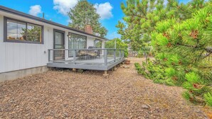 A modern house with a covered patio, a gravel driveway, and a pine tree. - Spacious Family Home with Bikes, Beach Toys, Grill, Workspace (Seaside)