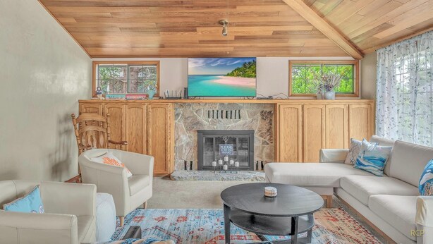 A cozy living room with a fireplace, a sofa, a coffee table, and a TV mounted above the fireplace. - Spacious Family Home with Bikes, Beach Toys, Grill, Workspace (Seaside)