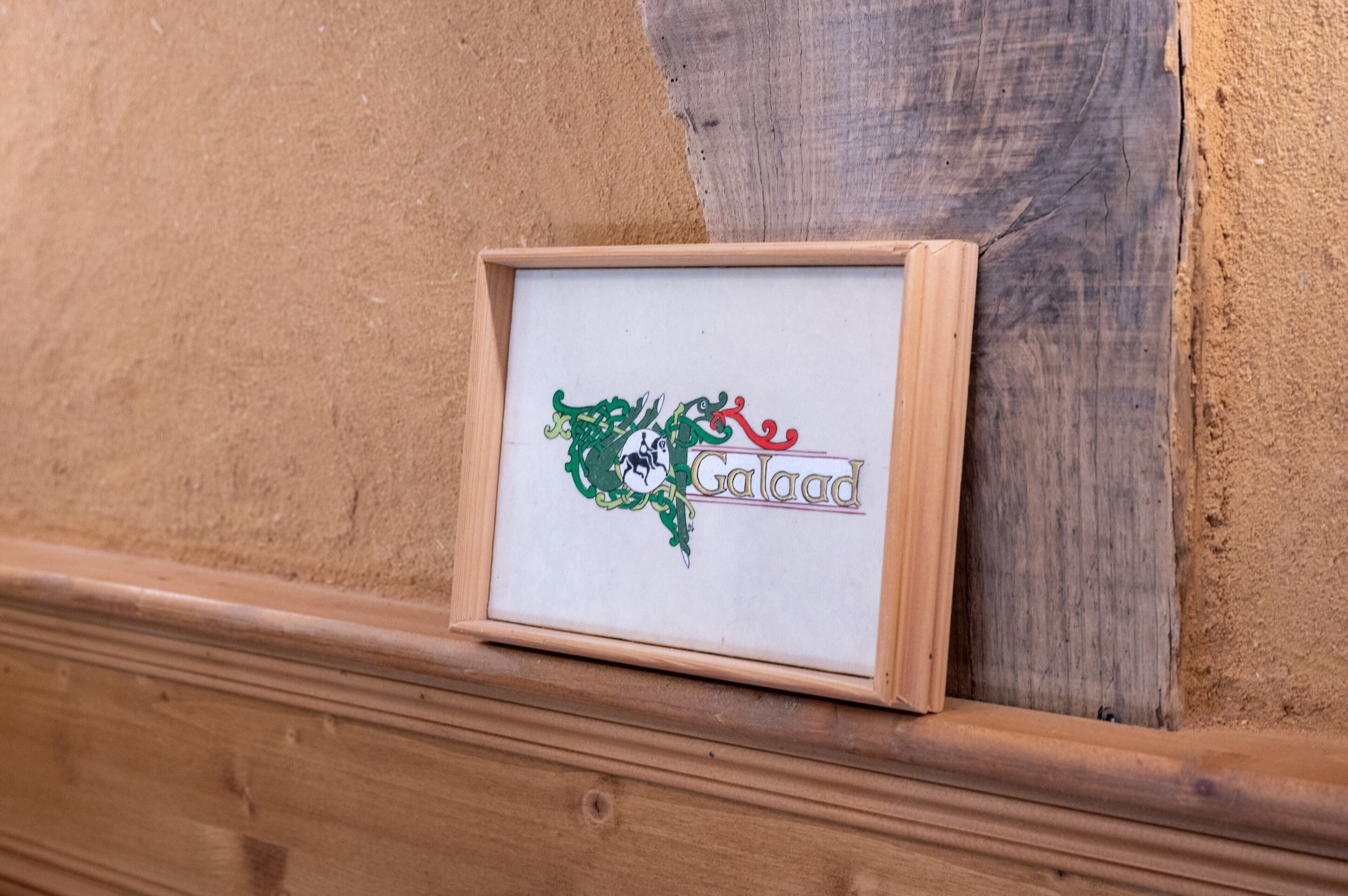 Een lijst met een logo en het woord 'Galad' op een houten wand.