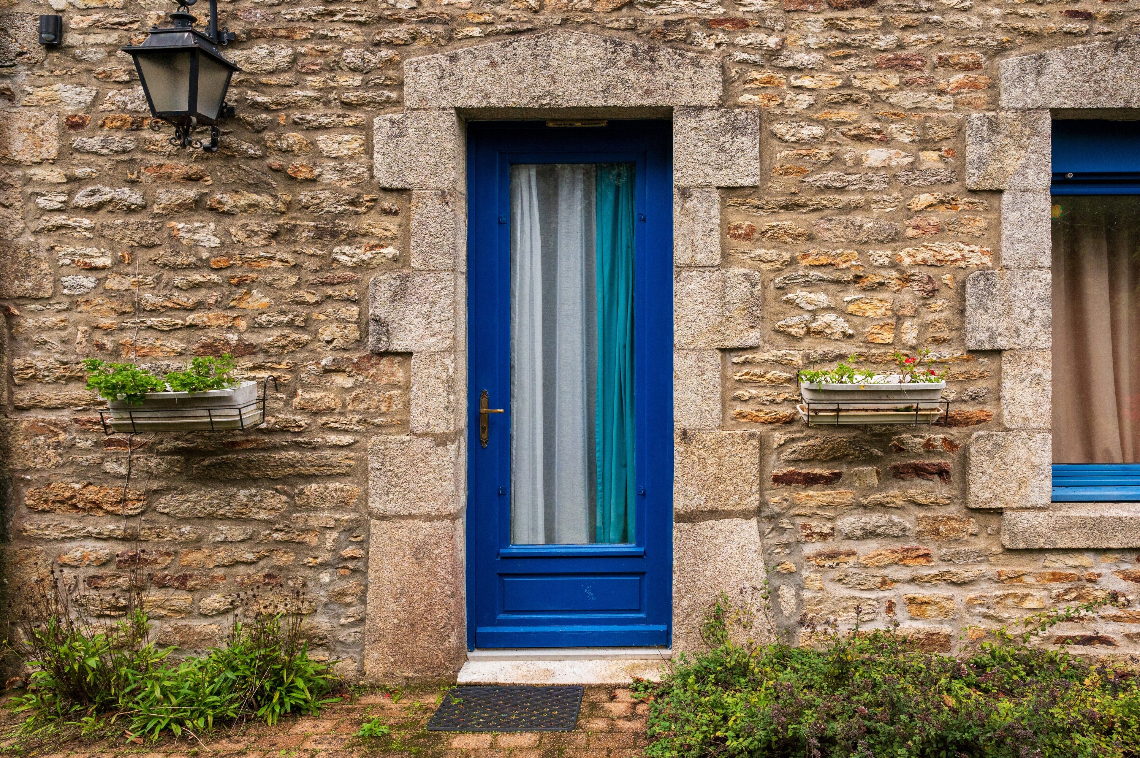 A stone building with a blue door, a window with a blue frame, and a hanging light fixture.