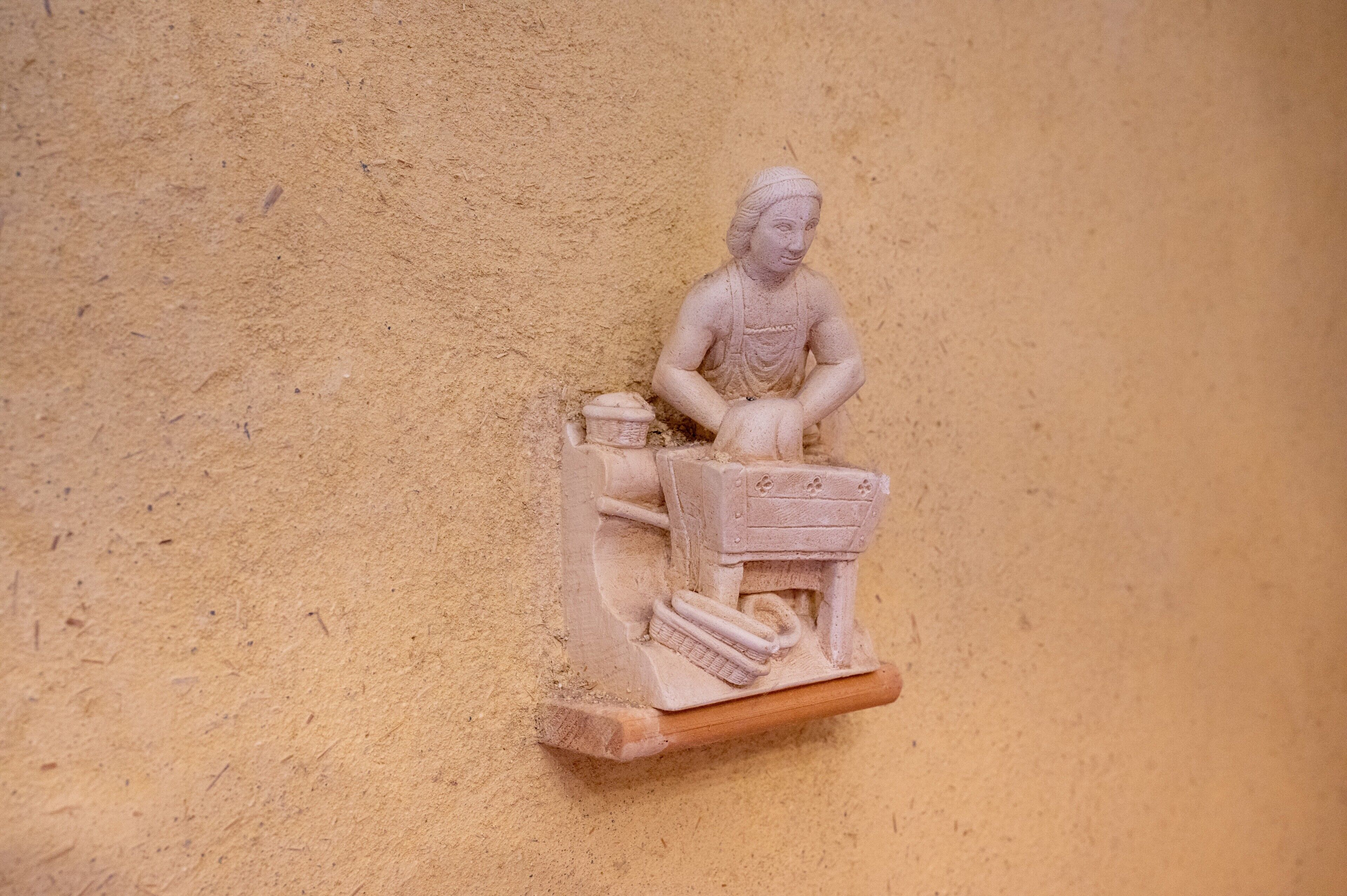 A relief sculpture of a seated figure with a tool on a wall.
