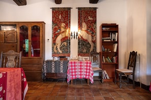 A room with a wooden cabinet, a table with a red and white checkered tablecloth, a bookshelf, and two tapestries depicting mythical creatures. - Bed and Breakfast 'Perceval' with Shared Terrace, Shared Garden and Wi-Fi (Pluvigner)