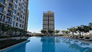 A swimming pool with lounge chairs and a tall building in the background. - Modern 1BR at Collective | Dubai Hills Mall Nearby (Dubai)