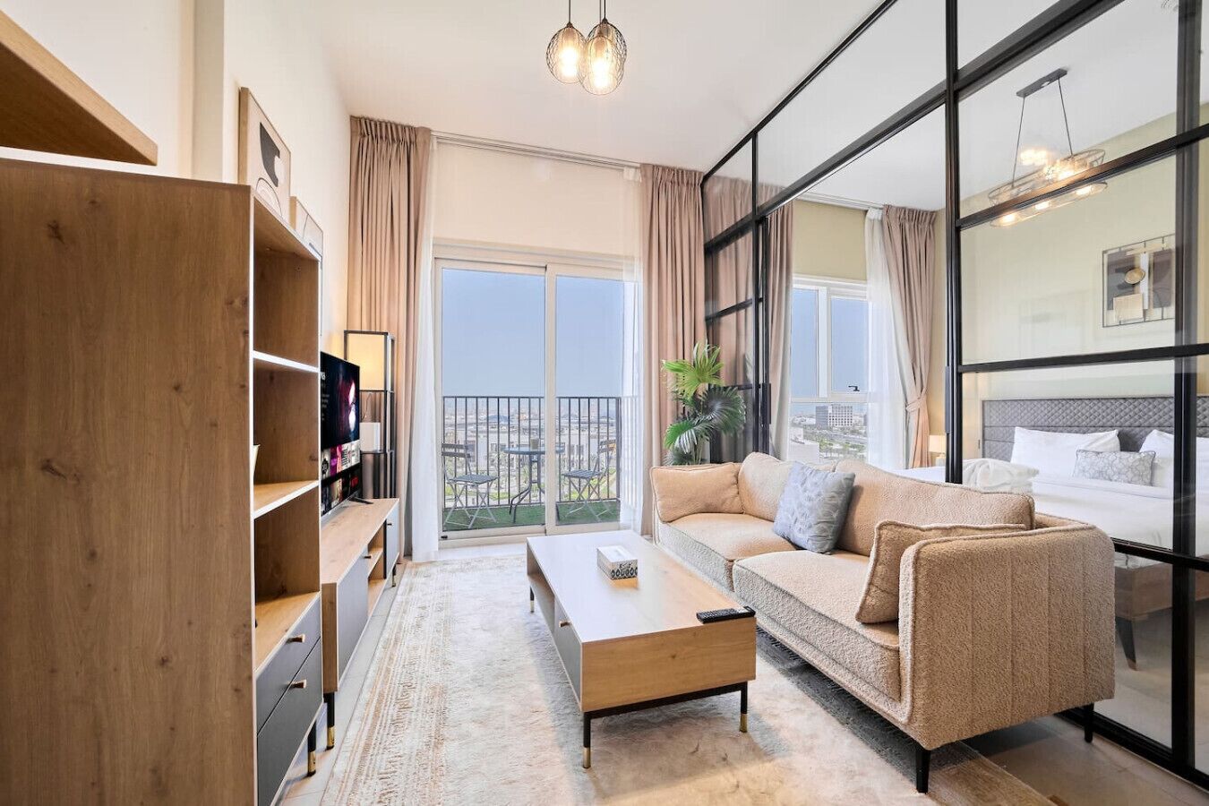 A modern living room with a sofa, coffee table, and TV, large windows with curtains, and a balcony with a city view.