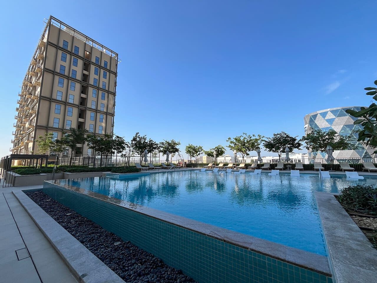 Una piscina con sillas de descanso y un edificio alto al fondo.