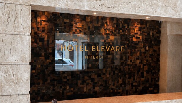 Un área de recepción con un muro de cristal que muestra el nombre del hotel, HOTEL ELEVARE NITEROI.