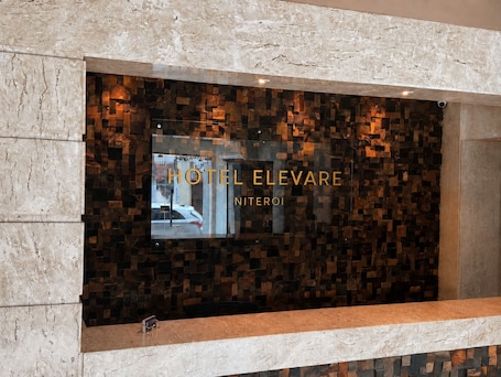 A reception area with a large digital display, a reception desk, and a wall with a mosaic pattern.. Hotel Elevare Niteroi