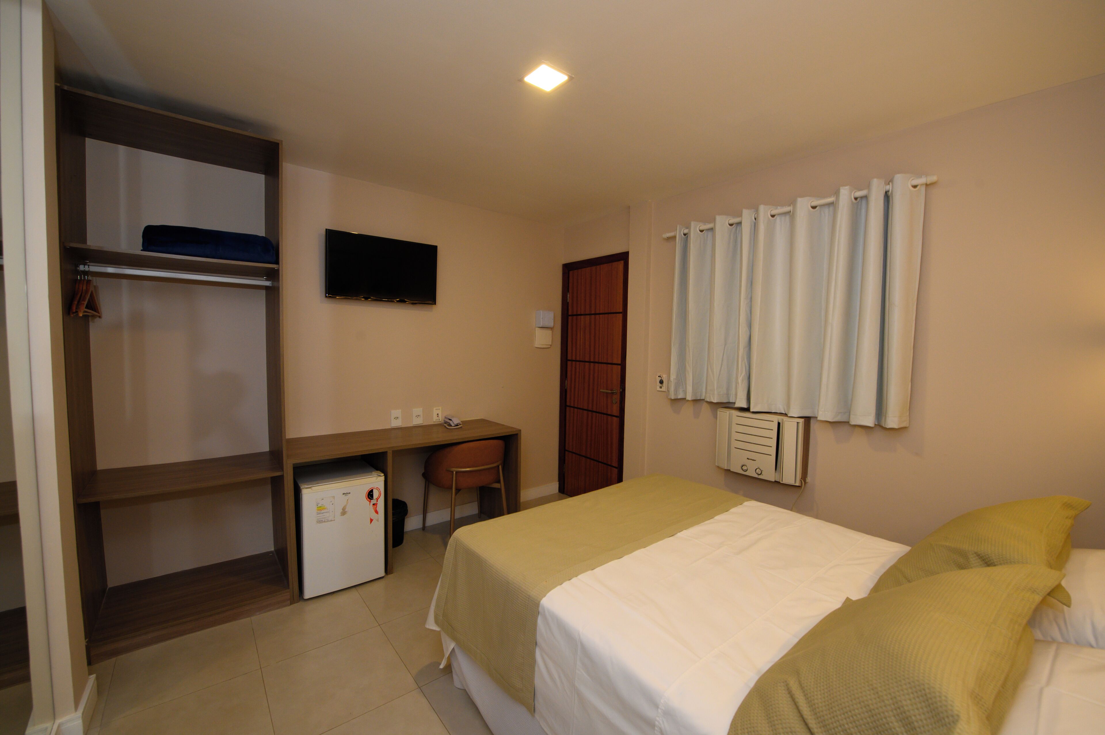 A bedroom with a bed, a desk, a wardrobe, and a television.