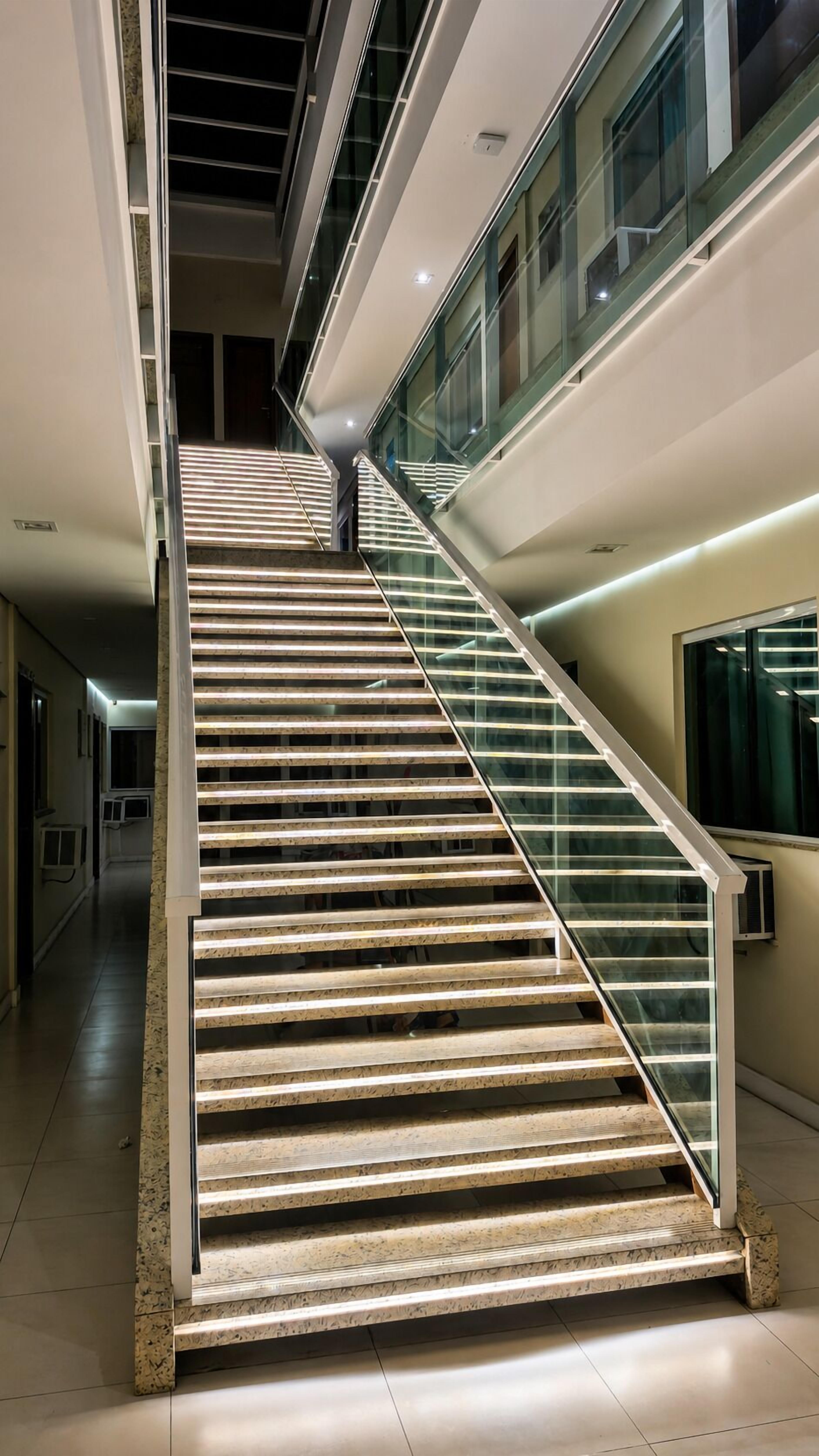Una escalera moderna con barandillas de cristal y peldaños iluminados, que sube a pisos superiores.