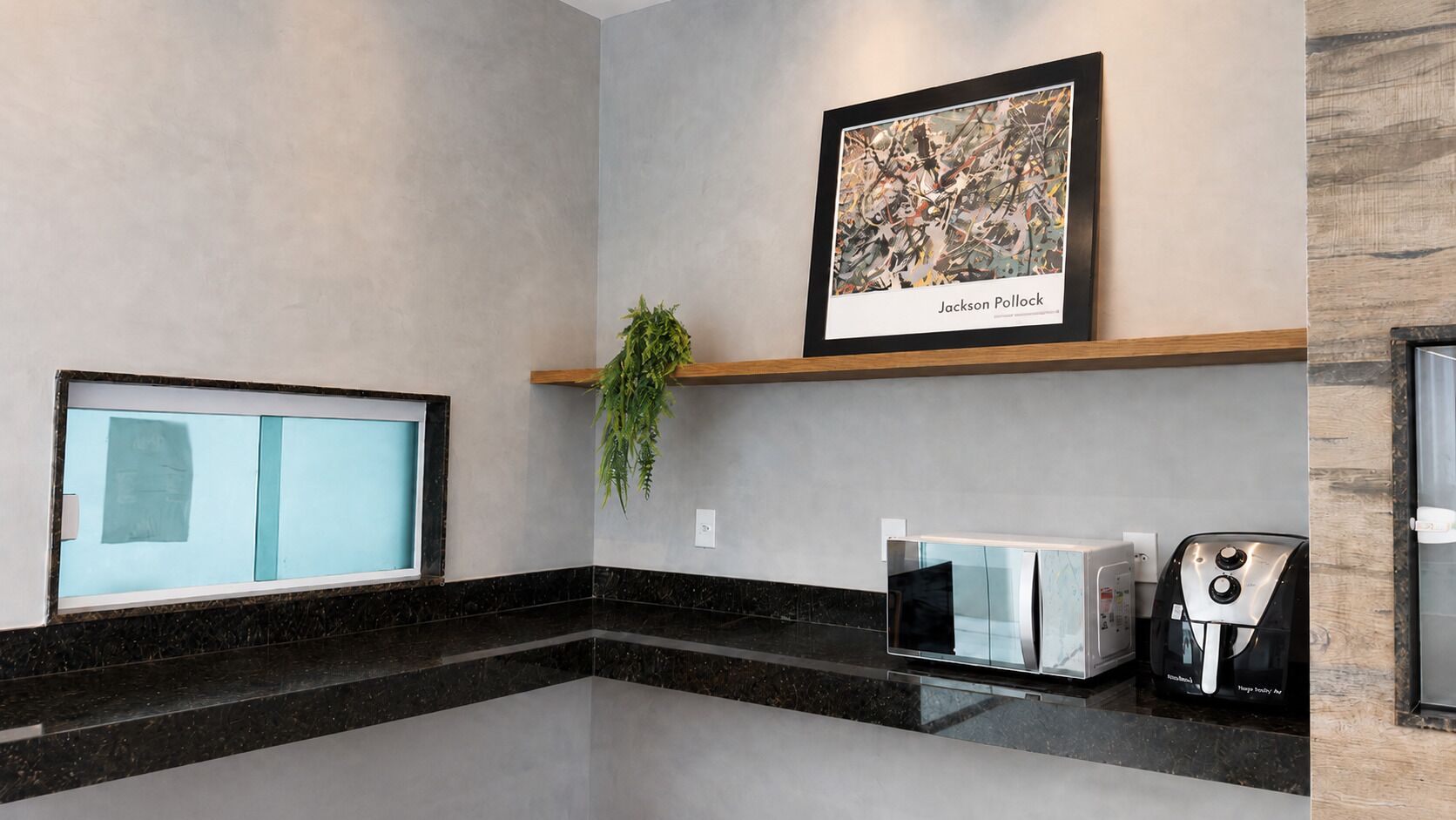 A modern kitchen with a countertop, a coffee machine, a microwave, and a framed artwork on the wall.