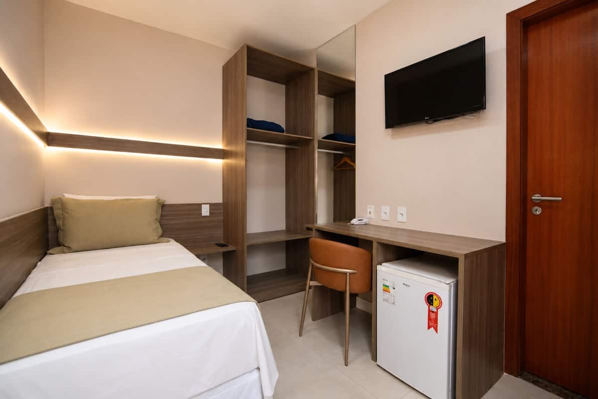 Een hotelkamer met een bed, een bureau, een stoel, een kledingkast, een televisietoestel en een koelkast.