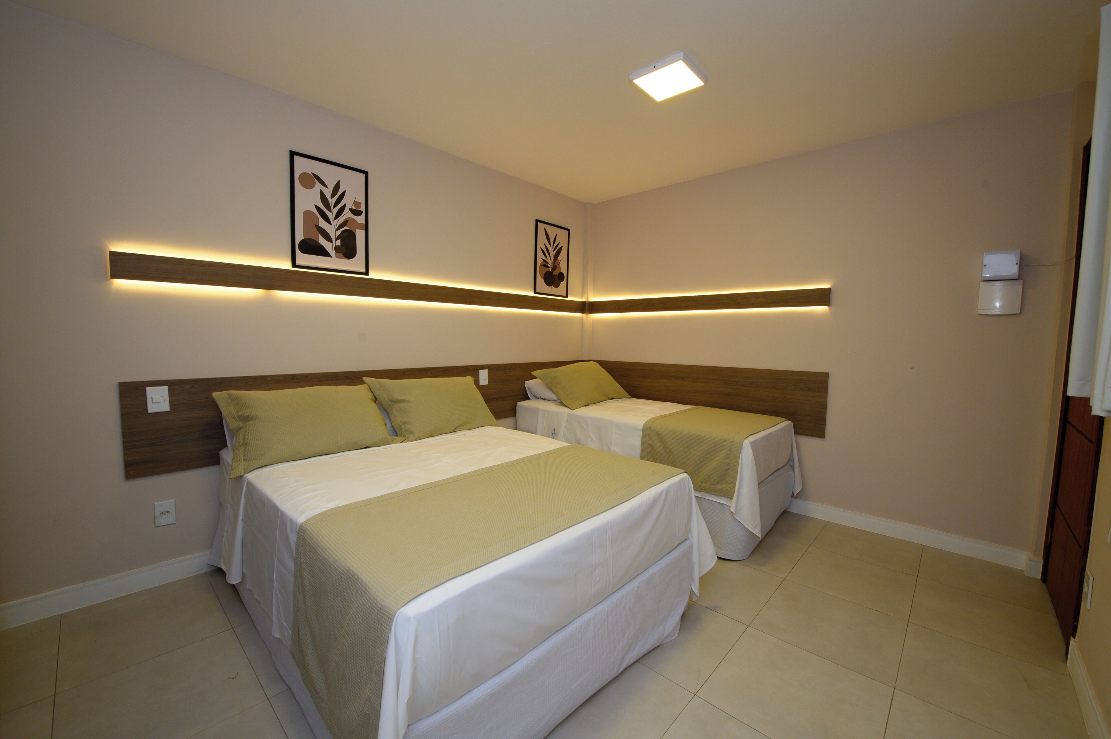 A hotel room with two beds, a wooden headboard, a ceiling light, and wall-mounted artwork.
