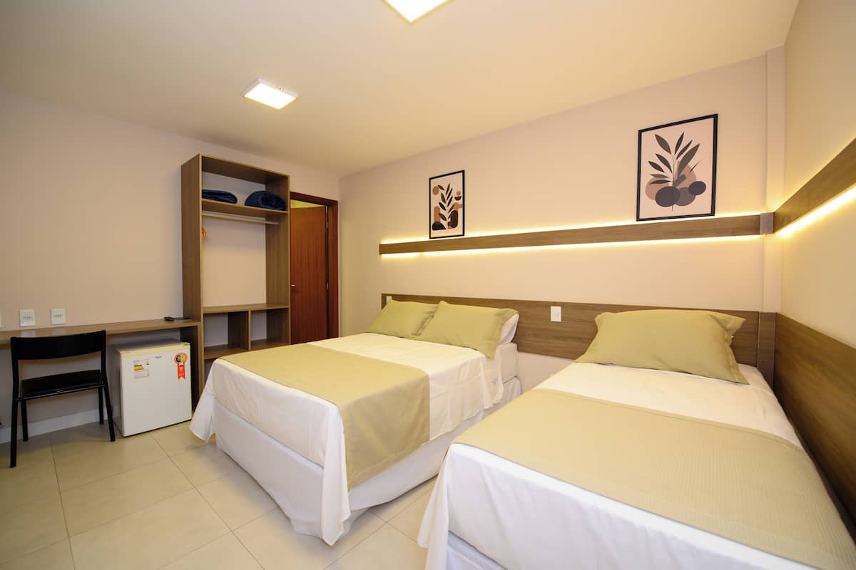 Een hotelkamer met twee bedden, een bureau, een koelkast en een kledingkast.
